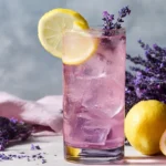 Iced lavender energy drink in a tall glass with lemon and fresh lavender on a marble counter.